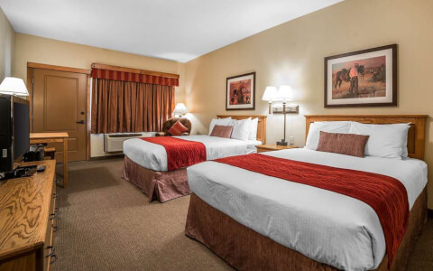 two queen beds in guest room with tv and table with two chairs
