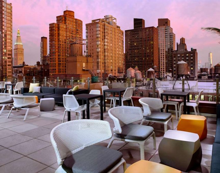 rooftoop lounge with dining area and views of new york city in pink sky