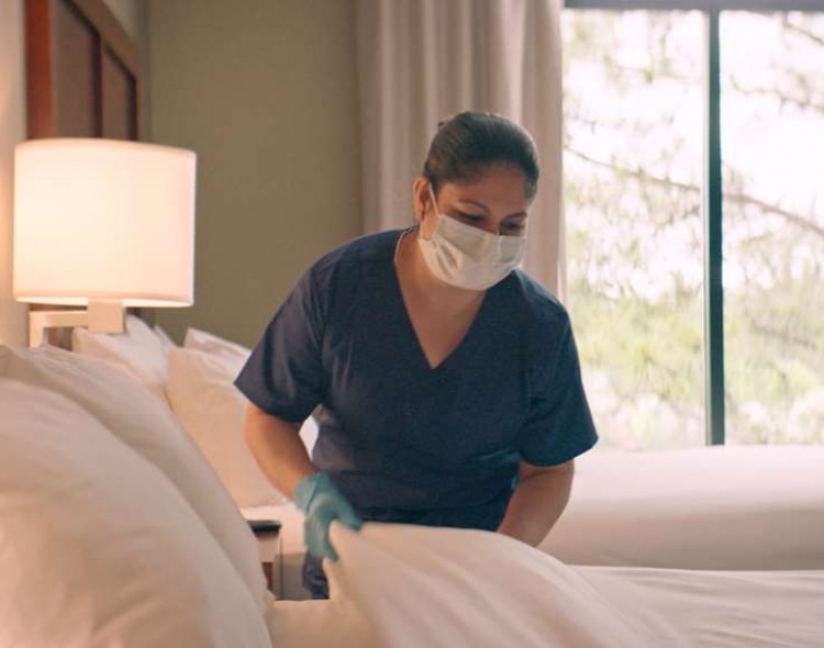 woman in mask and gloves making bed