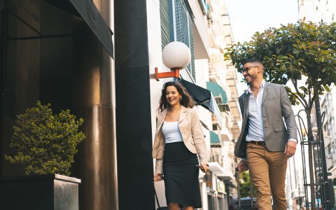 man and woman walking on sidewalk with luggage