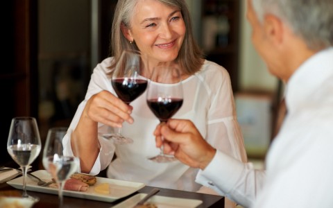 a couple clinks red wine glasses together over a dinner table