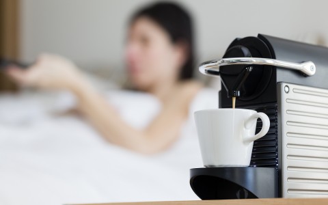 focused view of a nespresso machine with a woman in bed behind