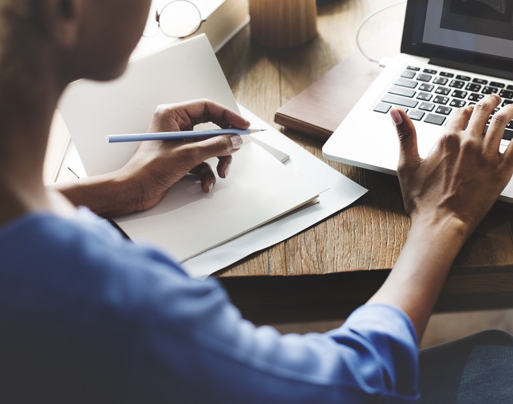 person writing in notebook and using laptop