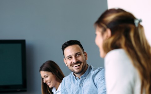 image of three people in a meeting and two of them are smiling and laughing with each other