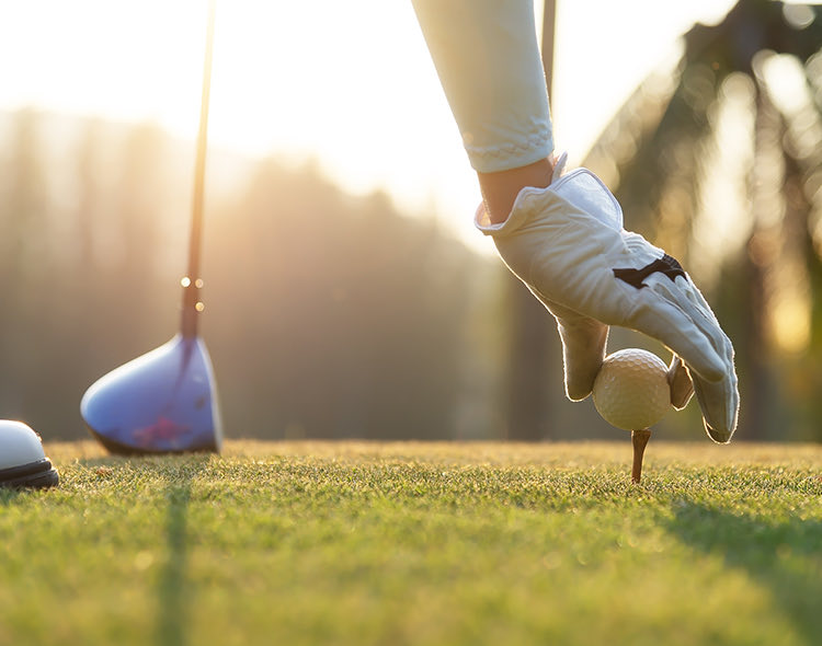 someone playing golf with gloves and a golf club as sun is setting