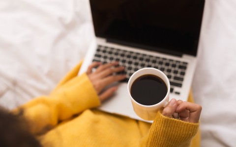 person in yellow sweater on laptop and holding cup of coffee