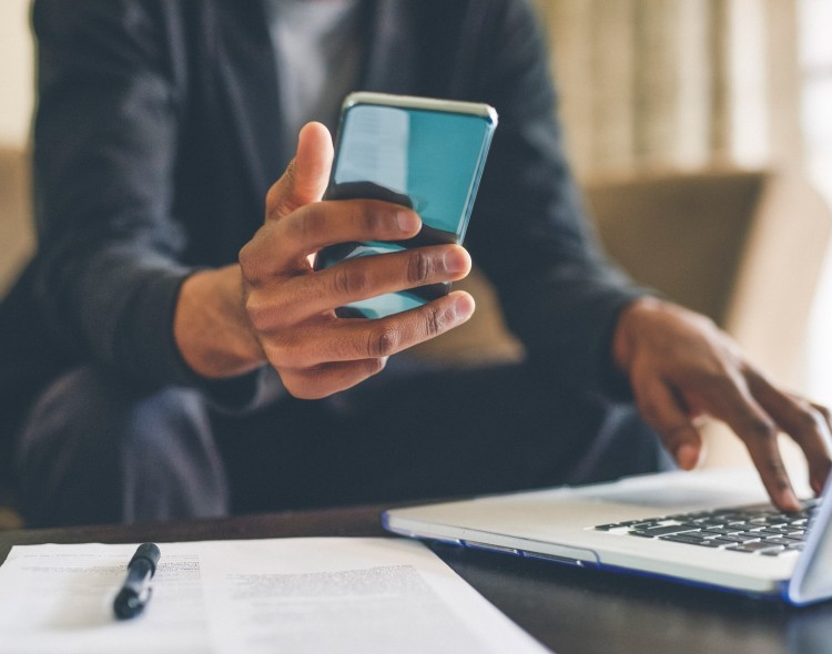 person holding their phone in one hand and using their other hand on their laptop