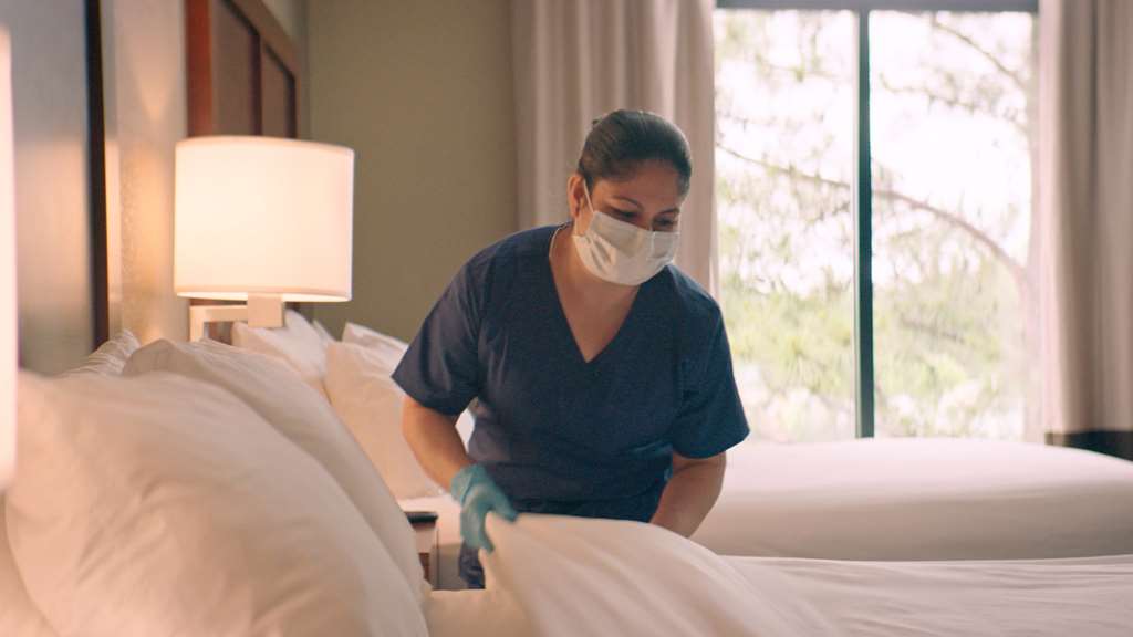 woman in face mask and gloves making bed