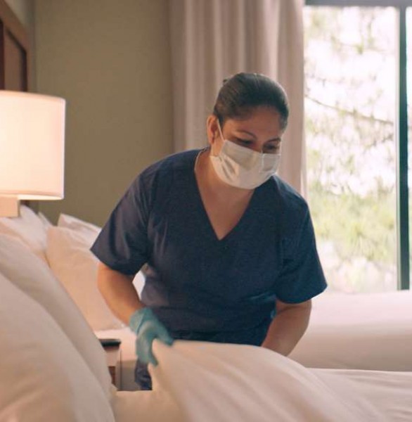 woman in face mask and gloves making bed