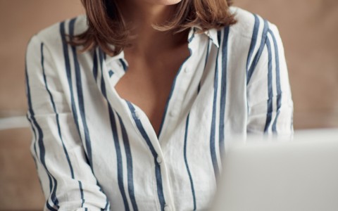 woman in white striped shirt smiling at laptop
