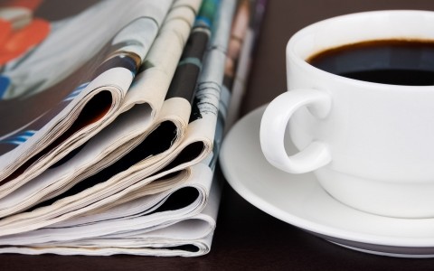 cup of coffee on plate next to stack of newspapers