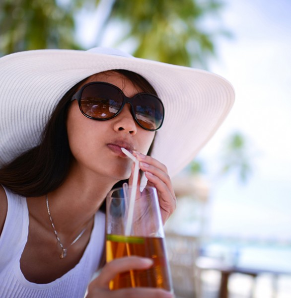 woman in floppy hat and sunglasses sipping on drink outside