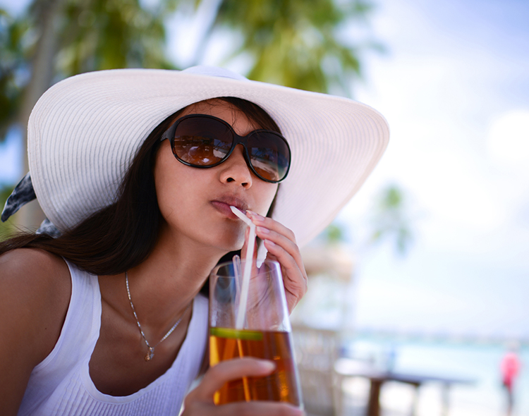 woman in floppy hat and sunglasses sipping on drink outside