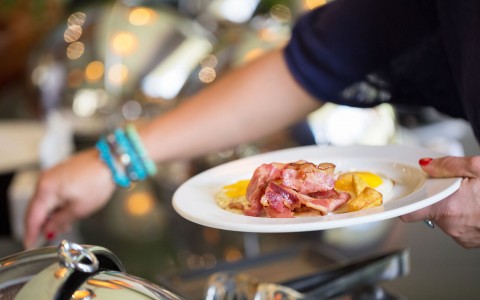 woman grabbing bacon and eggs from breakfast buffet
