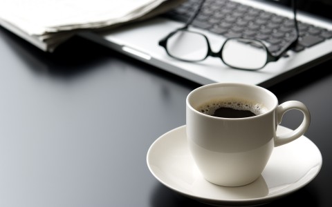 cup of hot coffee next to laptop and glasses