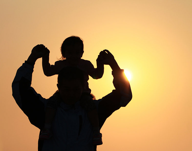 father holding child on shoulders during sunset