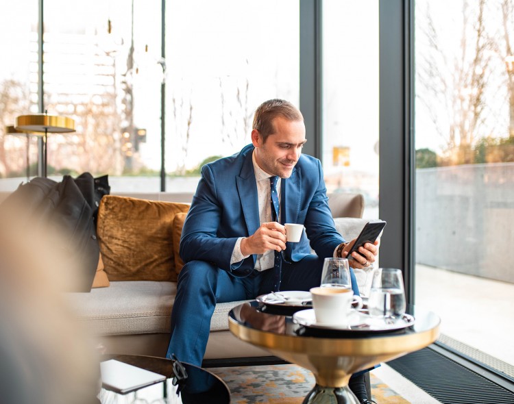 man sitting on couch looking at phone enjoying cup of espresso