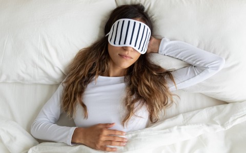 woman sleeping on white bed with striped eye mask on 