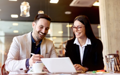 man and woman smiling doing work on computer