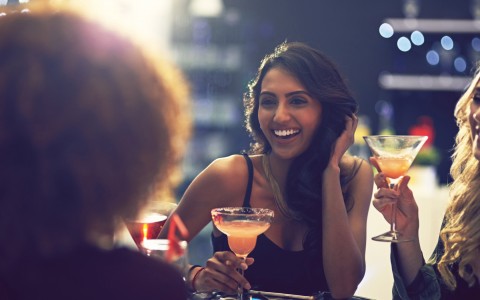 Young woman laughing looking at another woman while she is holding a margarita