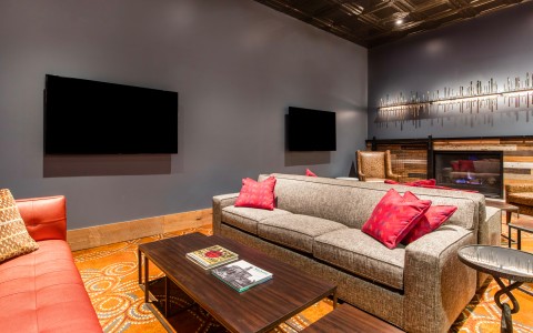 View of a stylish living room with two tvs on the wall, wooden tables and a comfy sofas 