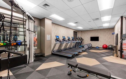 View of a small empty gym area with gym machine, tv on the wall and tools 