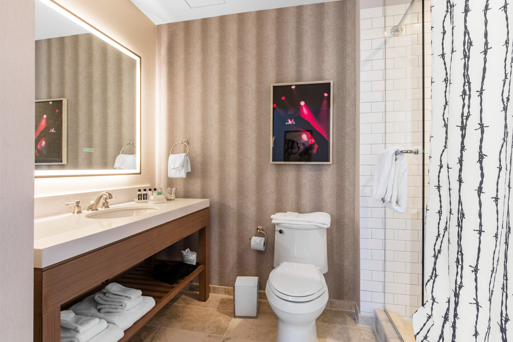 gallery View of a hotel washroom with features as a toilet, rectangular stylish mirror and some towels