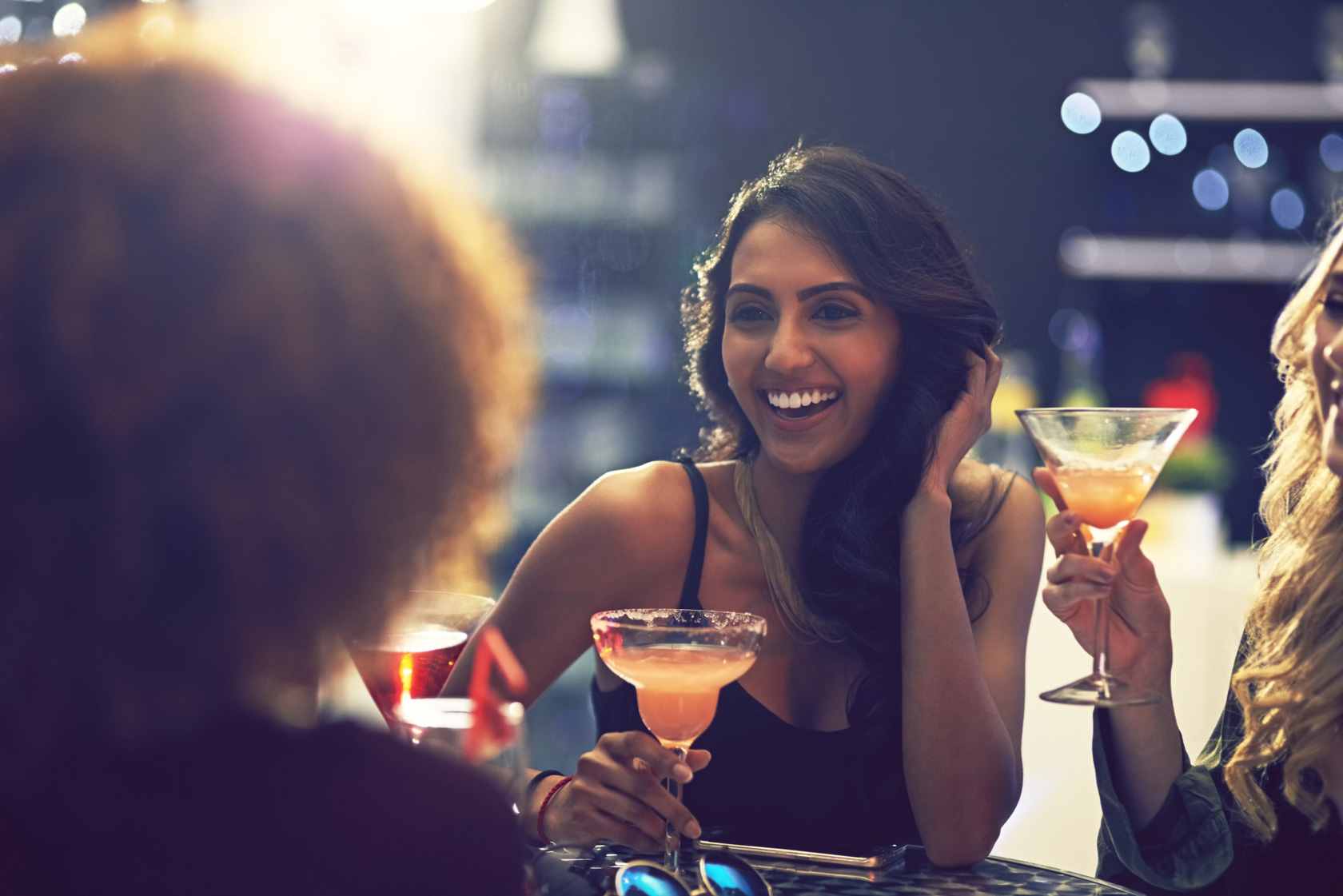 gallery Young woman laughing looking at another woman while she is holding a margarita