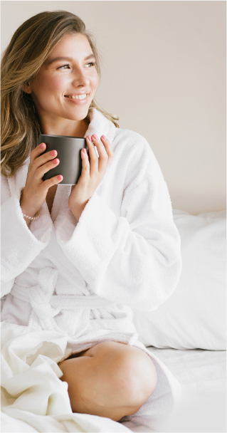Young woman sitting down in her bed looking forward while she is holding a cup of coffee