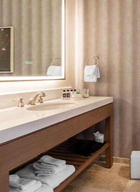 Washroom photographic with features as big mirror and a rectangular sink with some towels in it