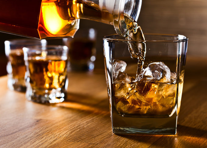 Close up view of a bottle filling a glass of a drink on the rocks