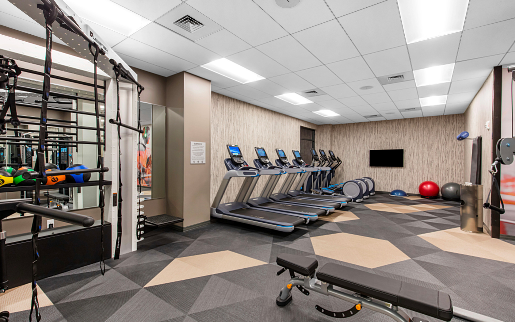 gallery View of a small empty gym area with gym machine, tv on the wall and tools 