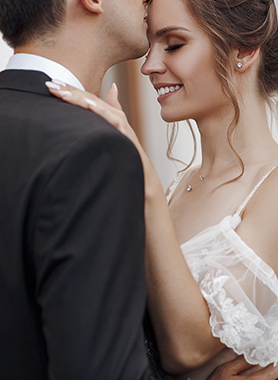 A groom kissing on the forehead bride while she is smiling