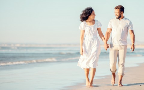 a couple walking by the beach holding hands and smiling