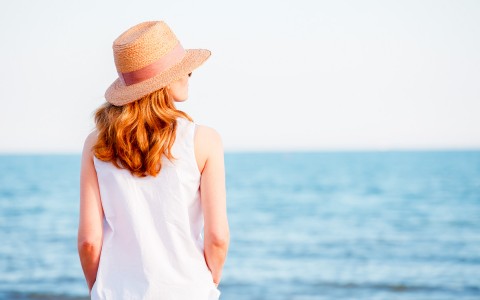 Redhaired woman wearing a sunhat overlooking the ocean.