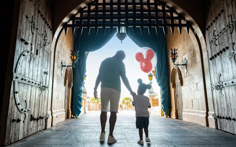 man and son walking through castle doors with mickey balloon