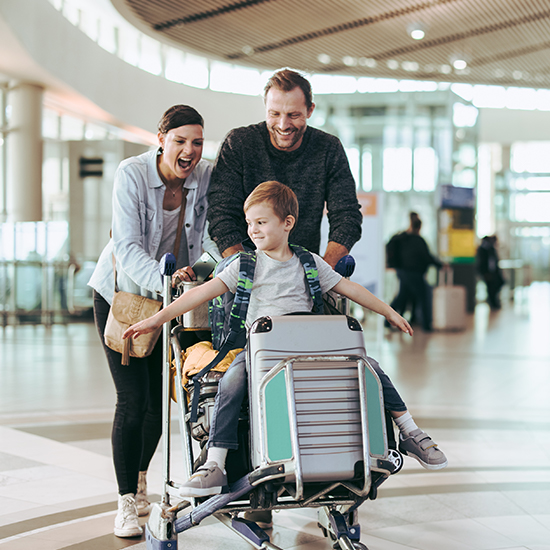 kid on luggage cart being pushed by parents at the airport