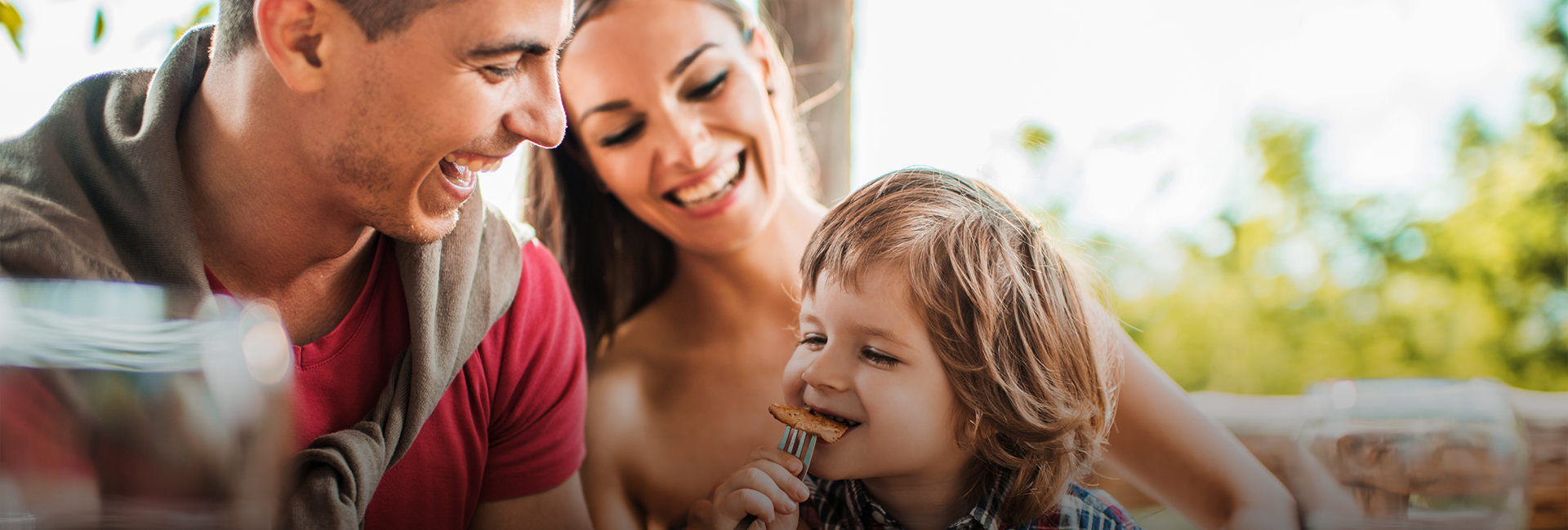 little boy biting slice of food with parents behind him