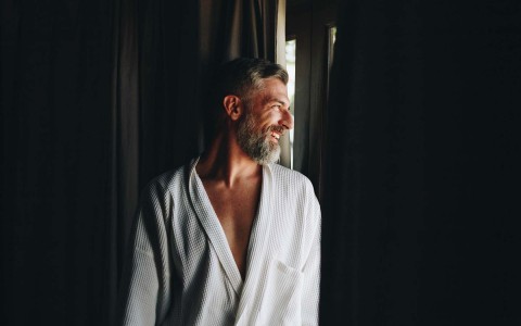 man with a robe looking through a window 