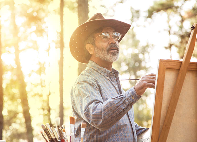 a man wearing a hat painting in the park