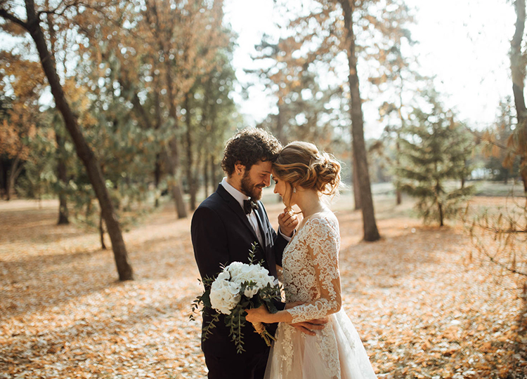 bride and groom getting their heads together and hugging in a park