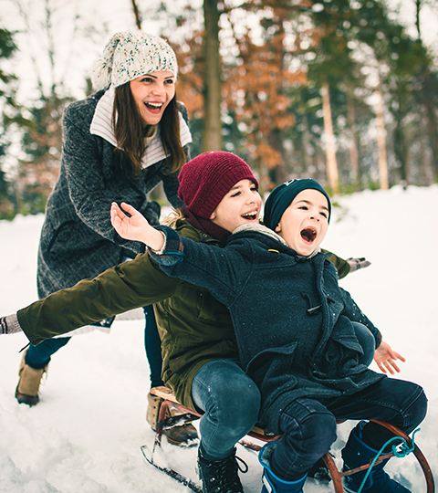 two children on a tiny sled in the snow as their mom pushes them