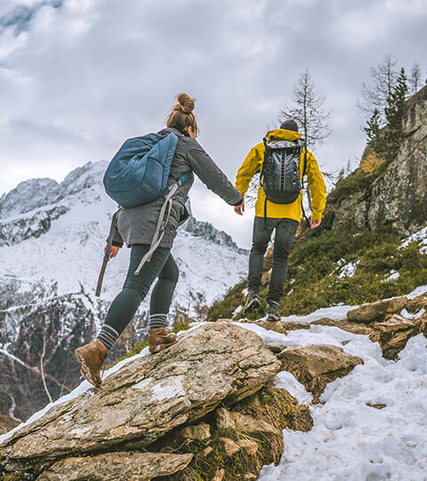 two people in hiking gear climbing on rocks in the snow 