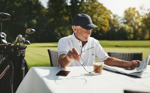 elderly guy reading and having a coffee at the golf curse 