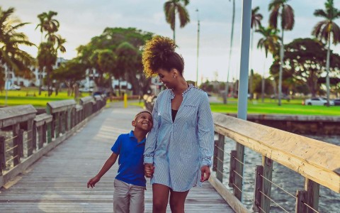 woman walking across the bridge and looking and holding a hand of a little boy 