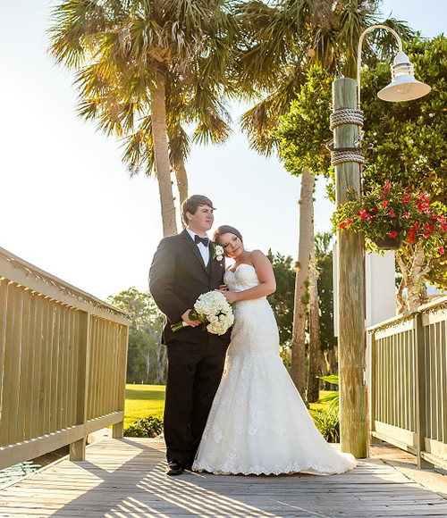 married couple in a wooden bridge looking to the right side while the guy is holding the boutique bride roses