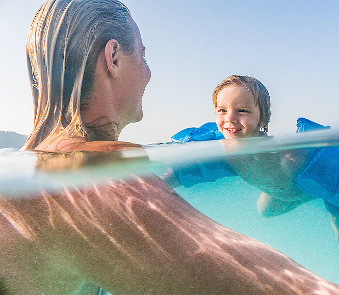 a little boy looking and smiling at this mom meanwhile he is swimming