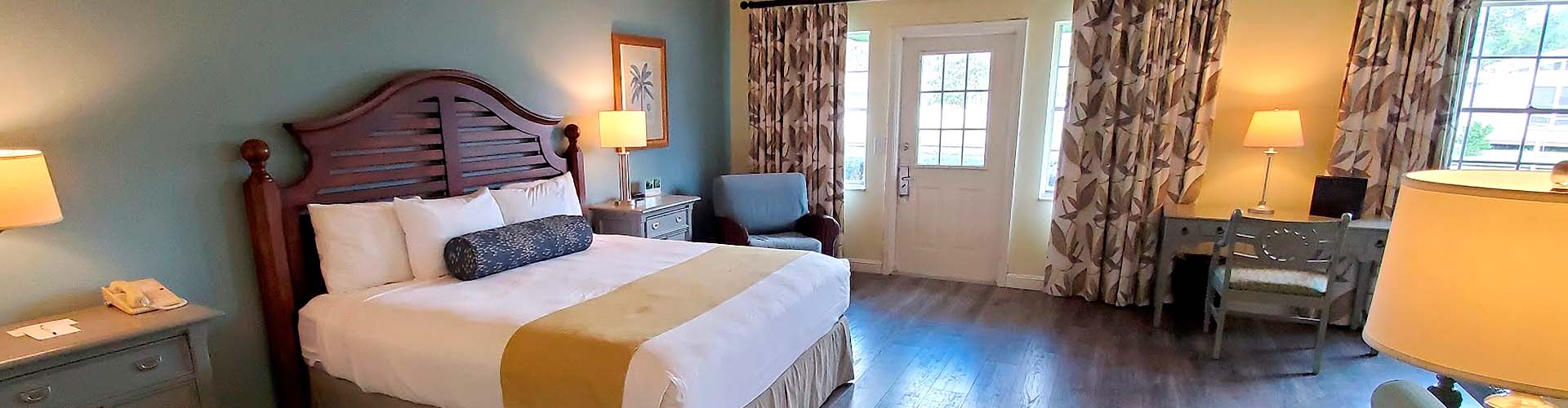 panoramic view of a hotel bedroom with features as a queen bed size, two nightstands and a simple study desk 