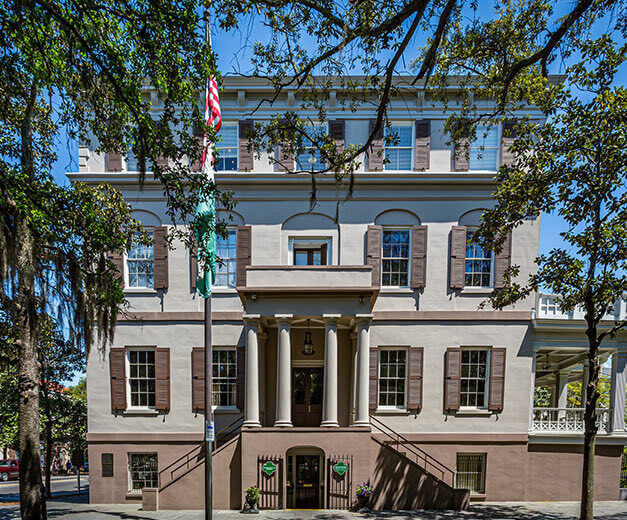 old historic building during the day with old trees and an american flag on a pole